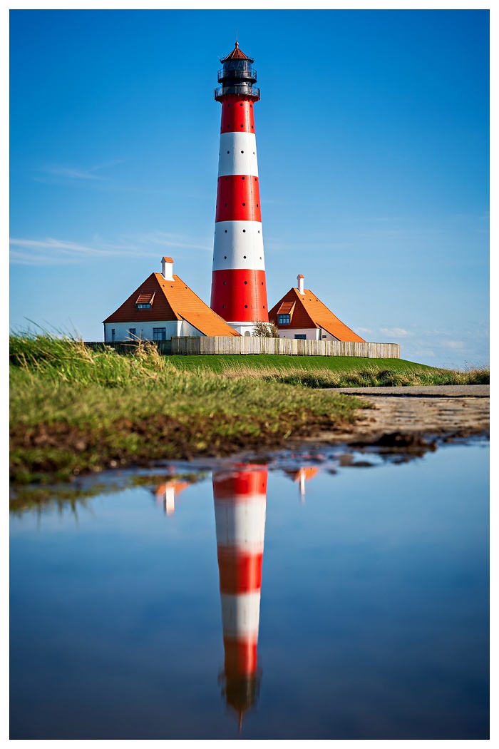 Blick auf den schicken Leuchtturm von Westerheversand an der Nordsee mit Spiegelung in einer Wasserpfütze