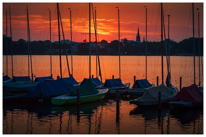 Rot schimmernder Sonnenuntergang mit Segelbooten am Rande der Außenalster in Hamburg