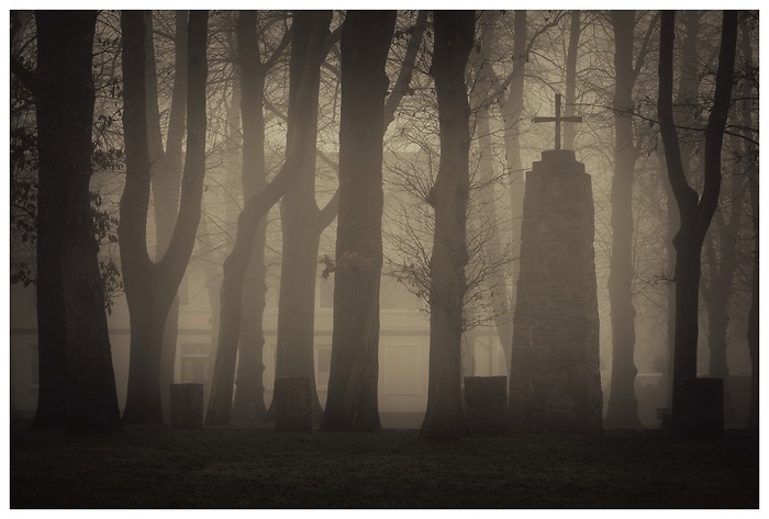 Blick auf einen großen Grabstein mit Kreuz im Nebel