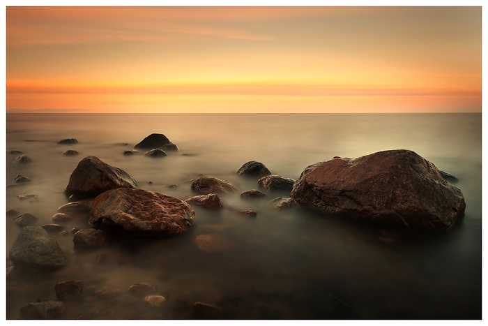 Roter Sonnenuntergang lässt Steine am Ostseestrand im Wassernebel verschwinden