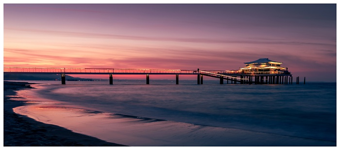 Blick auf den langen Steg zum Haus mit Spiegelung am Strand bei Sonnenuntergang